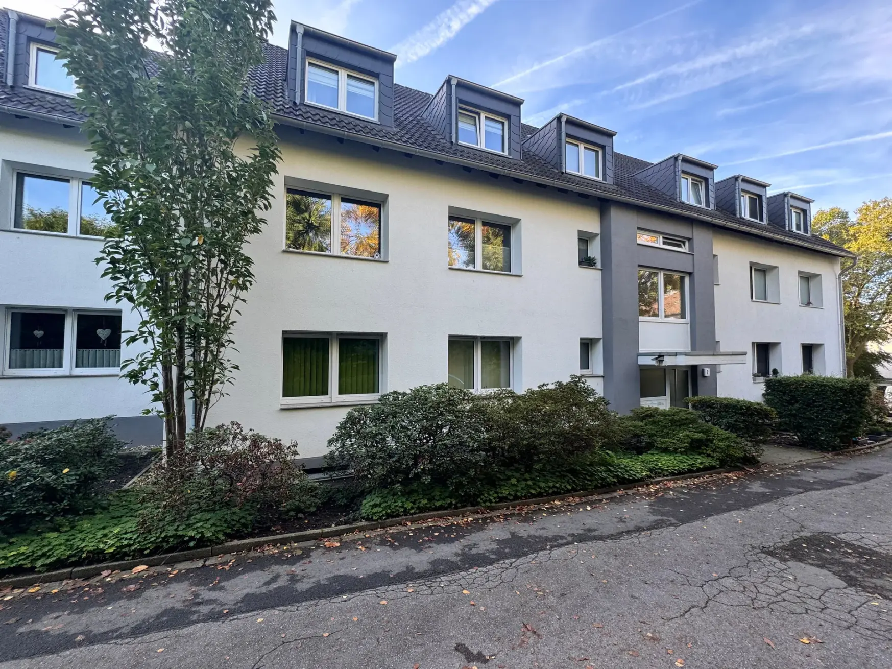 Helle Fassade eines Mehrfamilienhauses in Essen mit grau abgesetztem Eingang und Dachgauben